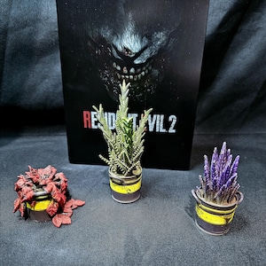 May include: Three small potted plants with different coloured leaves. The plants are in yellow and black containers. The background is a black poster with the words "Resident Evil 2" in red and white.
