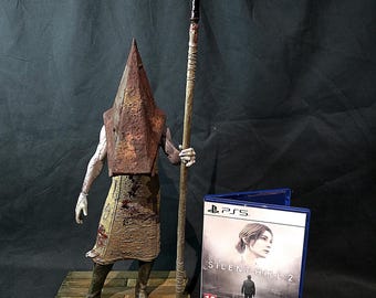May include: A detailed figurine of the Pyramid Head character from Silent Hill, holding a large spear. The figure stands on a wooden platform next to a PS5 game case for Silent Hill 2.