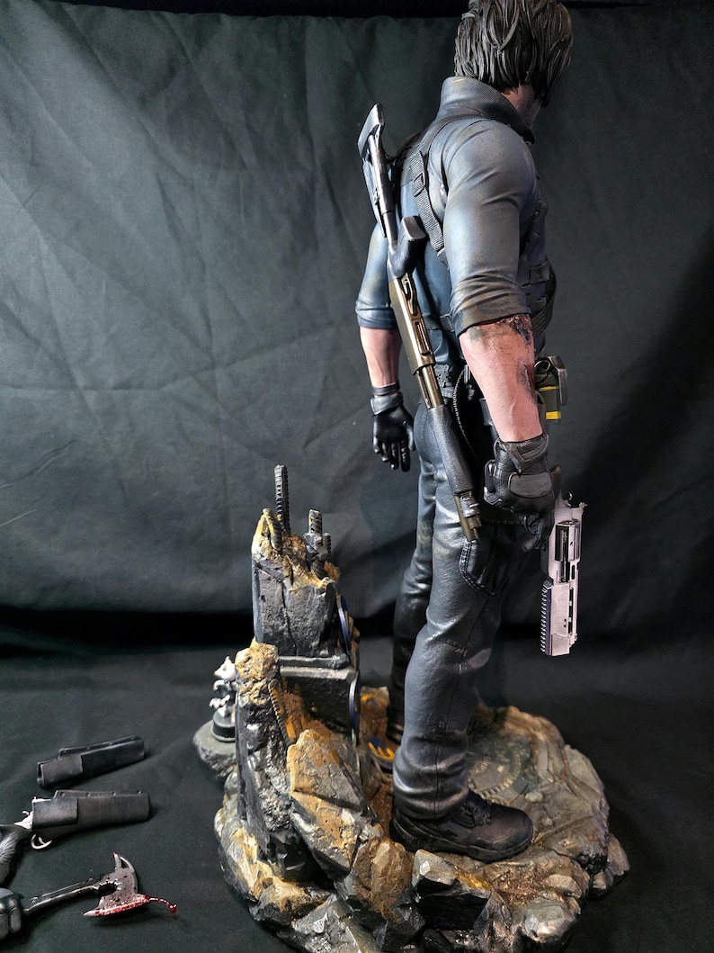 May include: A detailed figurine of a man in tactical gear, holding a pistol. He stands on a rocky base with additional weapons and accessories scattered around. The figure is dressed in black pants, a blue shirt, and black gloves.