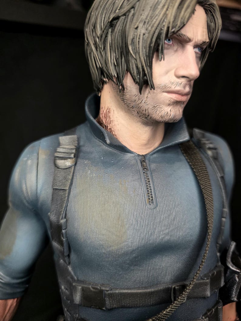 May include: A detailed figurine of a man with short, styled gray hair and blue eyes. He wears a blue-gray tactical shirt with a zipper and black straps. The figure has a serious expression and is set against a dark background.