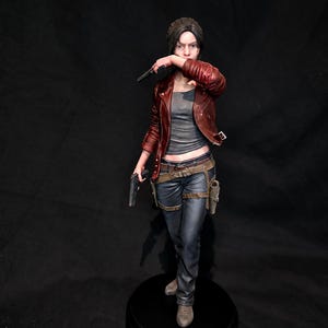 Può includere: Una statuetta dettagliata di un personaggio dai capelli scuri, che indossa una giacca di pelle rosso scuro sopra un top grigio, jeans blu con cintura marrone e una fondina. Il personaggio tiene una pistola nera in mano e una seconda vicino al viso.