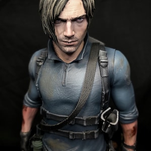 May include: A detailed figurine of a man with short, styled, light brown hair and a stern expression. He wears a blue tactical shirt with a black harness and utility belt. The figure has a realistic, weathered appearance, with visible details like a holster and a small grenade.