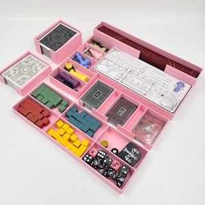 May include: Pink plastic organiser with compartments for storing game pieces and cards. The organiser includes dice, small wooden blocks, and cards with illustrations.
