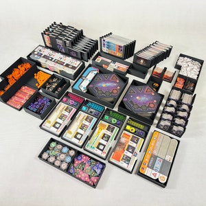 Könnte beinhalten: Ein Satz schwarzer Kunststoff-Aufbewahrungsboxen zum Organisieren von Brettspielkomponenten. Die Boxen sind mit verschiedenen farbigen Würfeln, Spielsteinen und Karten gefüllt. Die Boxen sind mit dem Namen des Spiels "Aeon's End" beschriftet.