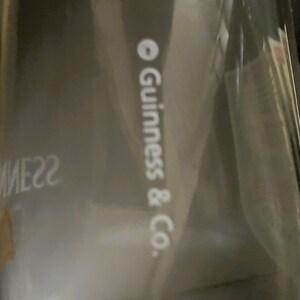 May include: A partially visible package with the text "Guinness & Co." in white. The packaging is clear, and the background is dark. The image is slightly out of focus.