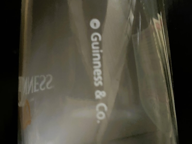 May include: A partially visible package with the text "Guinness & Co." in white. The packaging is clear, and the background is dark. The image is slightly out of focus.