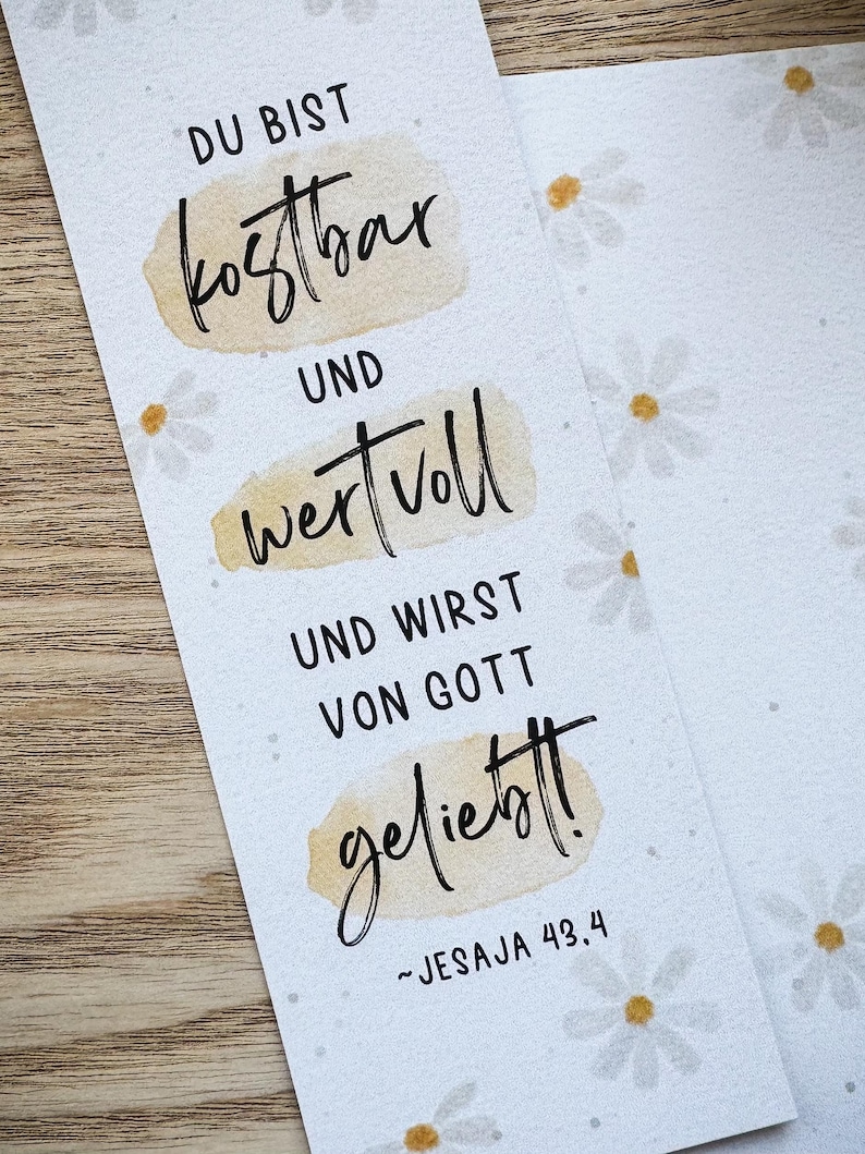 K&ouml;nnte beinhalten: Zwei wei&szlig;e Lesezeichen mit G&auml;nsebl&uuml;mchenmustern und deutschem Text. Der Text lautet "DU BIST kostbar UND wertvoll UND WIRST VON GOTT geliebt!" mit dem Verweis "~JESAJA 43,4". Der Text ist in schwarzer Schrift auf beigefarbenen Aquarellflecken.