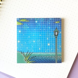 May include: A blue and green illustrated sticker with a starry night sky, a brick wall, a lamppost, and a few green bushes. The sticker has a grid pattern.