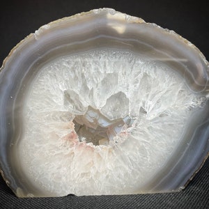 May include: A large, white agate geode with a natural opening revealing a crystal-lined interior. The geode has a grey and white banded exterior.