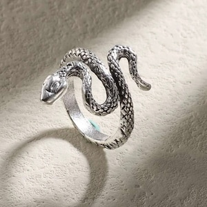 May include: A silver snake ring with a detailed design. The snake is coiled around the ring band, with its head facing forward.