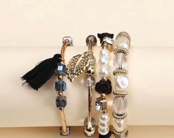 May include: Set of five gold-tone bracelets with various beads, including faux pearls, clear glass beads, and dark blue glass beads. One bracelet features a gold leaf charm and another has a black tassel.