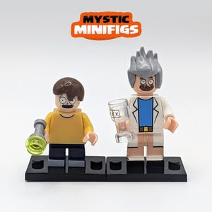 May include: Two custom Lego minifigures, one with brown hair and a yellow shirt holding a green and grey torch, and the other with grey hair and a white lab coat holding a clear glass with a drink inside. Both minifigures are standing on black Lego baseplates.