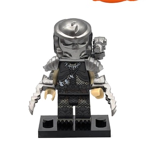 May include: A silver and black Lego minifigure of a Predator with a detailed helmet, a weapon, and a black base.
