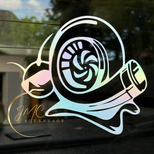 May include: A holographic sticker featuring a stylized turbocharger design in the shape of a snail. The sticker has a pearlescent finish that reflects a rainbow of colors. The text "JMC ADVANTAGE" is in a gold circle.