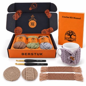 May include: A crochet kit in an orange and black box containing three 50g yarn balls in earthy brown, sage green, and shadowed silver. Includes a manual, two crochet hooks sized 4.0mm and 5.0mm, a mug with a lavender cozy, and crocheted items.