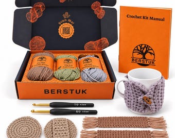 May include: A crochet kit in an orange and black box containing three 50g yarn balls in earthy brown, sage green, and shadowed silver. Includes a manual, two crochet hooks sized 4.0mm and 5.0mm, a mug with a lavender cozy, and crocheted items.