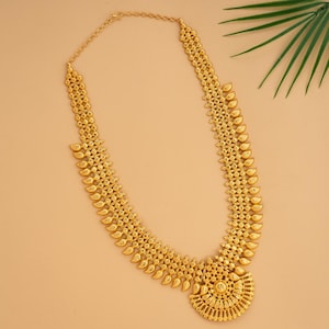 May include: A gold-colored necklace with a detailed design. The necklace features a series of connected leaf-shaped pendants and a circular pendant at the bottom. The chain is visible at the top, and the necklace is set against a neutral background.