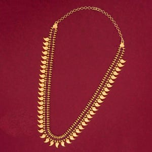 May include: A gold-colored necklace with a series of small, leaf-shaped pendants and a line of small, red gemstones. The necklace is set against a solid red background. The chain is made of small, connected circles.