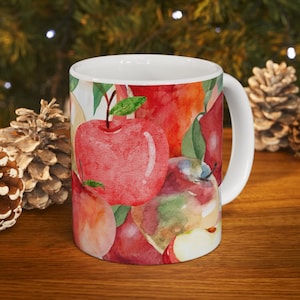 May include: White ceramic mug with a watercolor design of red apples and green leaves. The mug has a white handle.