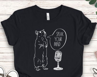 May include: Black t-shirt with a white graphic of a rat holding a microphone and a speech bubble that says "Speak Your Mind".