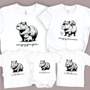 May include: A set of four white t-shirts featuring black and white illustrations of capybaras. The shirts have the text "capypapa", "capymama", "littlebara", and "babybara" printed on them.