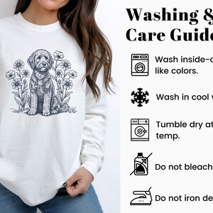 Pode incluir: Camisola branca com uma ilustra&ccedil;&atilde;o a preto e branco de um c&atilde;o rodeado por flores. A parte superior de manga comprida tem gola redonda. A imagem tamb&eacute;m inclui um guia de lavagem e cuidados.