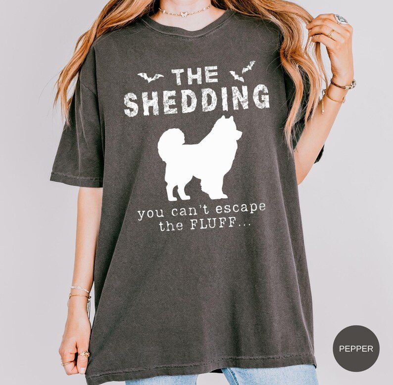 May include: Dark gray t-shirt with white text and a dog silhouette. The text reads "THE SHEDDING" above the dog and "you can't escape the FLUFF..." below. Two bat silhouettes are above the word "SHEDDING".