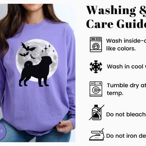K&ouml;nnte beinhalten: Ein violettes Langarmshirt mit einer schwarzen Silhouette einer M&ouml;pse vor einem Vollmond, Flederm&auml;usen und Sternen. Das Shirt hat ein violettes Logo mit der Aufschrift "VIOLET". Wasch- und Pflegehinweise sind ebenfalls enthalten.