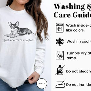 Op de afbeelding: Witte sweatshirt met een zwart-wit illustratie van een Corgi hond die een boek leest, met de tekst "just one more chapter...". De was- en verzorgingsgids staat aan de rechterkant.