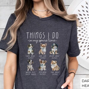 Op de afbeelding: Donkergrijze heather t-shirt met de tekst "THINGS I DO - in my spare time" en afbeeldingen van puppy's. Het shirt vermeldt activiteiten zoals "Think About Puppies" en "Watch Cute Puppy Videos".