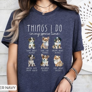 Op de afbeelding: Marineblauwe t-shirt met de tekst "THINGS I DO - in my spare time-" en illustraties van puppy's. Het shirt vermeldt activiteiten zoals "Think About Puppies" en "Watch Cute Puppy Videos."