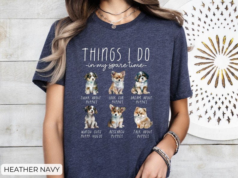Op de afbeelding: Marineblauwe t-shirt met de tekst "THINGS I DO - in my spare time-" en illustraties van puppy's. Het shirt vermeldt activiteiten zoals "Think About Puppies" en "Watch Cute Puppy Videos."