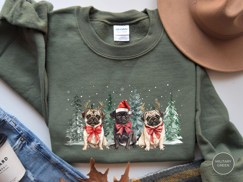 May include: A green Christmas sweatshirt with a design of three pugs wearing Santa hats and reindeer antlers. The pugs are standing in front of a snowy forest scene.