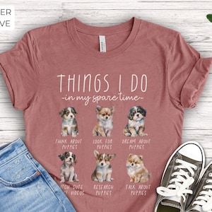 Op de afbeelding: Heather mauve t-shirt met de tekst "THINGS I DO - in my spare time-" en illustraties van puppy's. Het shirt zegt ook "THINK ABOUT PUPPIES", "LOOK FOR PUPPIES", "DREAM ABOUT PUPPIES", "WATCH CUTE PUPPY VIDEOS", "RESEARCH PUPPIES" en "TALK ABOUT PUPPIES".