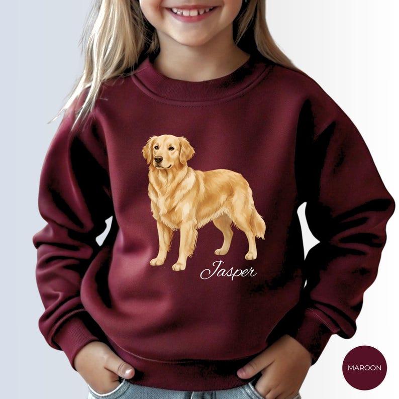 May include: Maroon sweatshirt featuring a golden retriever illustration. The dog is standing, with the name "Jasper" in script below. The sweatshirt is a solid maroon color, with a small maroon circle with the word "MAROON" in white text.