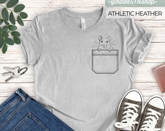 May include: A gray t-shirt with a pocket featuring a black and white illustration of a mouse peeking out of the pocket. The text "ATHLETIC HEATHER" is printed on the shirt.