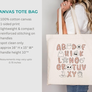 May include: A natural-colored cotton canvas tote bag featuring a Halloween-themed alphabet graphic. The letters are filled with an orange and white checkered pattern, interspersed with illustrations of ghosts, pumpkins, skulls, and witch hats.