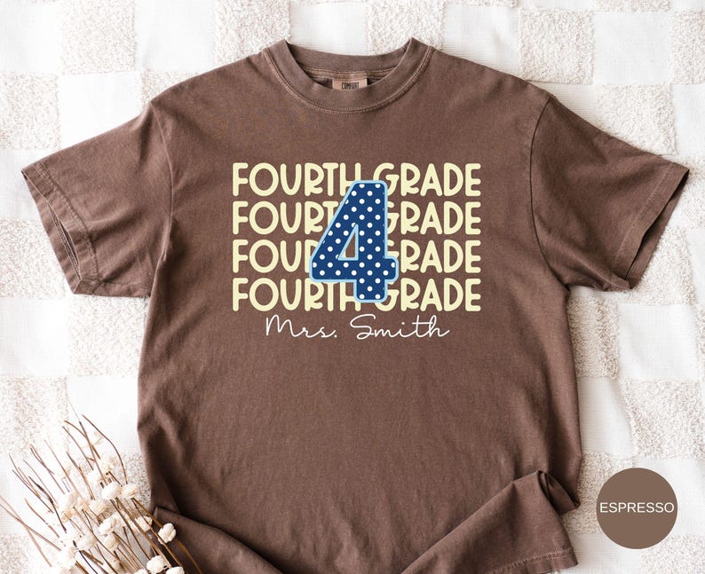 May include: A brown short-sleeve t-shirt featuring the text FOURTH GRADE repeated four times in light yellow. A large dark blue number 4 with white polka dots is centered over the text. The name Mrs. Smith is printed in white cursive below.