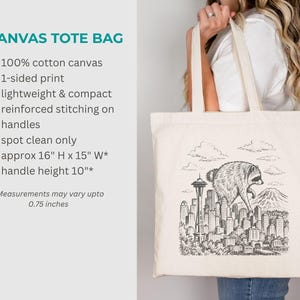 Pu&ograve; includere: Una borsa tote in tela color naturale con un'illustrazione a inchiostro nero di un procione che cammina sopra lo skyline di una citt&agrave; che include lo Space Needle e una montagna. La borsa ha due manici e misura circa 40,6 cm per 38,1 cm.