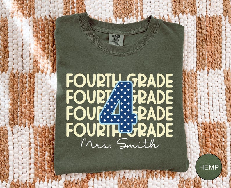 May include: An olive green crew neck t-shirt featuring the repeating text FOURTH GRADE in a light yellow font. A large dark blue number 4 with white polka dots is centered over the text. The name Mrs. Smith is printed in white script below.