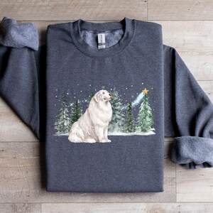 May include: Dark grey heather sweatshirt featuring a white dog sitting in front of a winter scene with evergreen trees and a star. The sweatshirt has rolled-up sleeves and a crew neck.