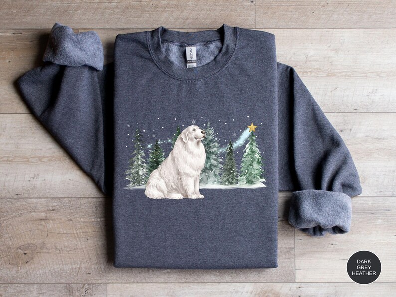 May include: Dark grey heather sweatshirt featuring a white dog sitting in front of a winter scene with evergreen trees and a star. The sweatshirt has rolled-up sleeves and a crew neck.