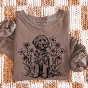 Pode incluir: Camiseta de manga comprida cor espresso com gola redonda. Apresenta uma ilustra&ccedil;&atilde;o em preto e branco de um c&atilde;o sentado entre flores. A palavra "Espresso" est&aacute; em um c&iacute;rculo no canto inferior direito.