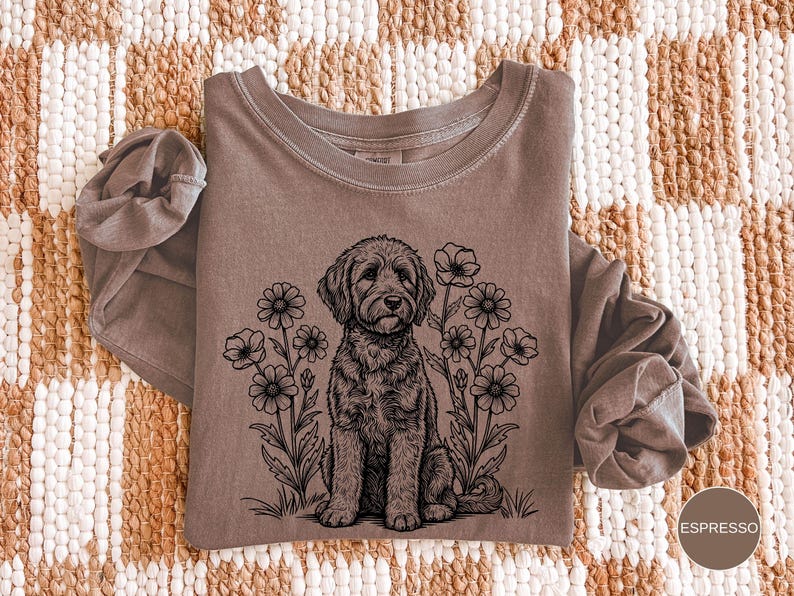 Pode incluir: Camiseta de manga comprida cor espresso com gola redonda. Apresenta uma ilustra&ccedil;&atilde;o em preto e branco de um c&atilde;o sentado entre flores. A palavra "Espresso" est&aacute; em um c&iacute;rculo no canto inferior direito.