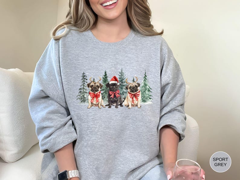 May include: A gray sweatshirt with a Christmas-themed design featuring three pugs wearing Santa hats and reindeer antlers. The pugs are standing in front of a snowy forest scene.
