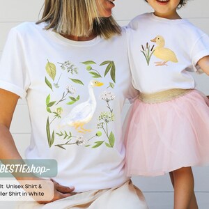 May include: White t-shirt with a watercolor illustration of a goose and floral details. The text "yourBESTIEShop" is printed on the bottom of the shirt.  Adult Unisex Shirt & Toddler Shirt in White.