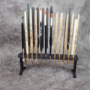 May include: A black metal stand with 18 paint brushes of various colours and lengths. The brushes are arranged in a row, with the handles facing up.