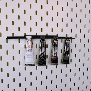 May include: Four tubes of paint are hanging on a pegboard wall. The tubes are labeled "Winton Oil Colour", "502 Abt&ouml;nung", and "502 Abt&ouml;nung".