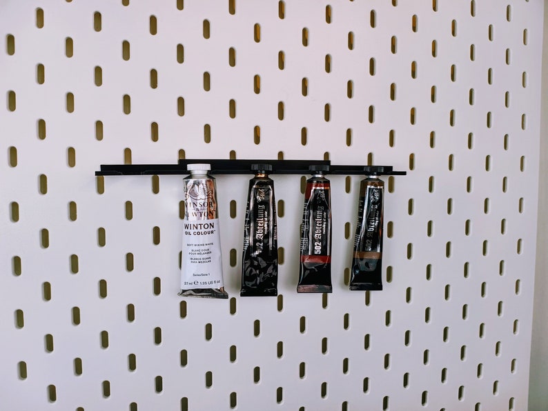 May include: Four tubes of paint are hanging on a pegboard wall. The tubes are labeled "Winton Oil Colour", "502 Abt&ouml;nung", and "502 Abt&ouml;nung".