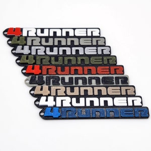 May include: A set of 4Runner keychains in various colors, including white, gray, black, green, tan, and red. The keychains are made of plastic and have a 3D printed design.